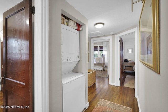 washroom featuring stacked washer and dryer, dark wood-type flooring, laundry area, baseboards, and attic access