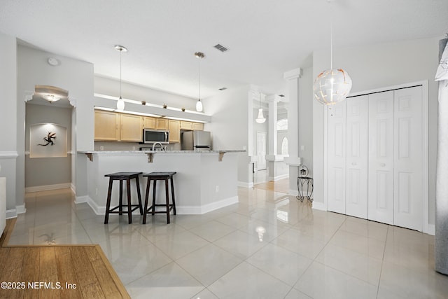 kitchen featuring light brown cabinets, a peninsula, a kitchen breakfast bar, freestanding refrigerator, and stainless steel microwave