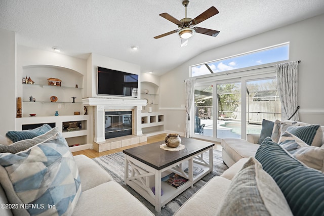 living area with a textured ceiling, lofted ceiling, built in shelves, a fireplace, and wood finished floors