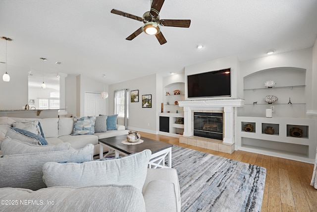 living room featuring a textured ceiling, a tile fireplace, wood finished floors, built in features, and vaulted ceiling