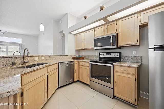 kitchen with light brown cabinets, light stone counters, stainless steel appliances, and a sink