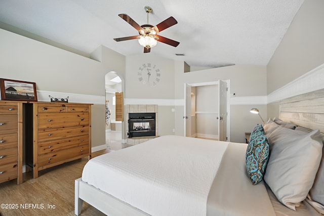 bedroom featuring visible vents, vaulted ceiling, a textured ceiling, wood finished floors, and a tile fireplace