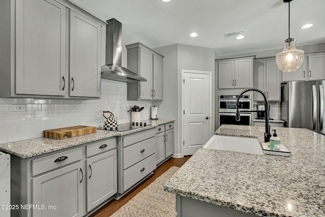 kitchen with appliances with stainless steel finishes, gray cabinets, dark wood-style floors, wall chimney exhaust hood, and tasteful backsplash