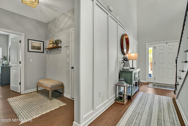 entrance foyer featuring a towering ceiling, stairs, baseboards, and dark wood-type flooring