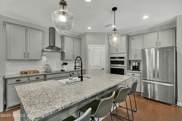 kitchen with light stone counters, tasteful backsplash, gray cabinetry, appliances with stainless steel finishes, and wall chimney range hood