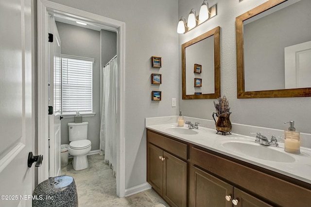 bathroom featuring baseboards, a sink, toilet, and double vanity