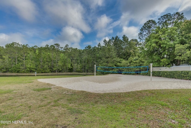 view of community with volleyball court, a yard, and a view of trees