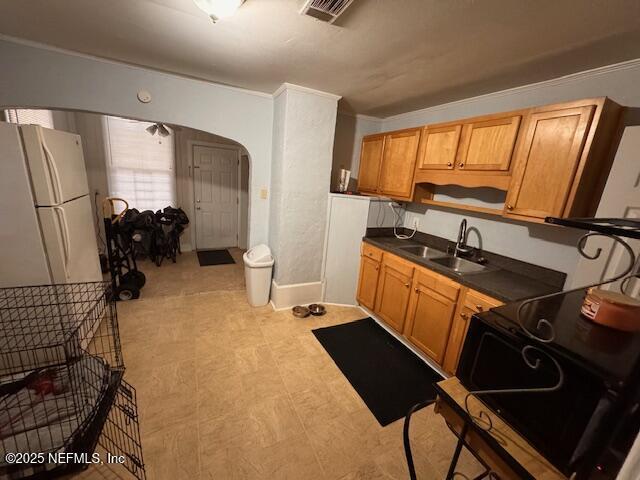 kitchen with arched walkways, a sink, visible vents, freestanding refrigerator, and dark countertops