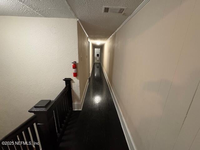 hallway with visible vents, ornamental molding, dark wood-style flooring, a textured ceiling, and an upstairs landing