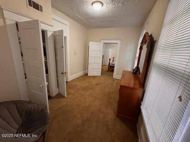 corridor featuring baseboards, carpet, visible vents, and a textured ceiling