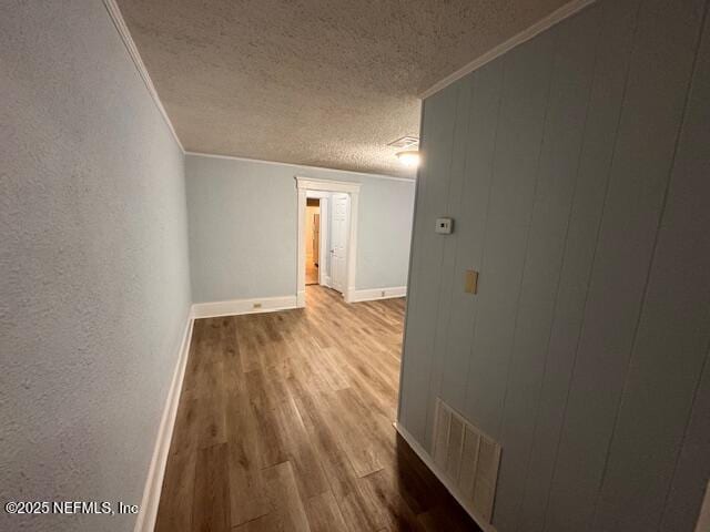 empty room featuring crown molding, light wood finished floors, visible vents, a textured ceiling, and baseboards