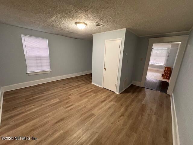 unfurnished room featuring visible vents, a textured ceiling, baseboards, and wood finished floors