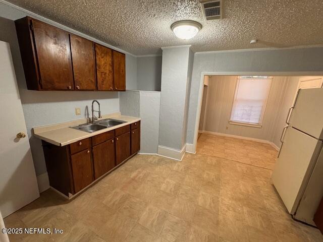 kitchen featuring dark brown cabinetry, freestanding refrigerator, light countertops, crown molding, and a sink