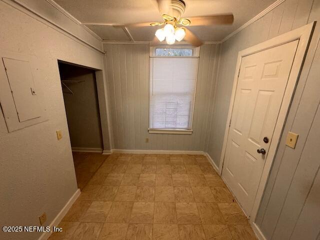 interior space with electric panel, crown molding, wooden walls, and baseboards