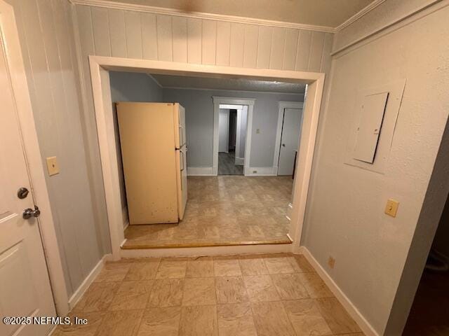 hall with crown molding, baseboards, and wooden walls