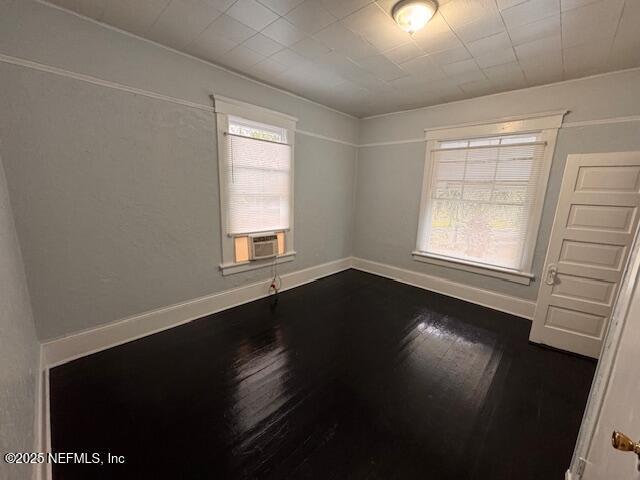 empty room with baseboards, plenty of natural light, wood finished floors, and cooling unit