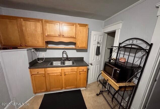 kitchen with brown cabinets, crown molding, dark countertops, a sink, and black microwave