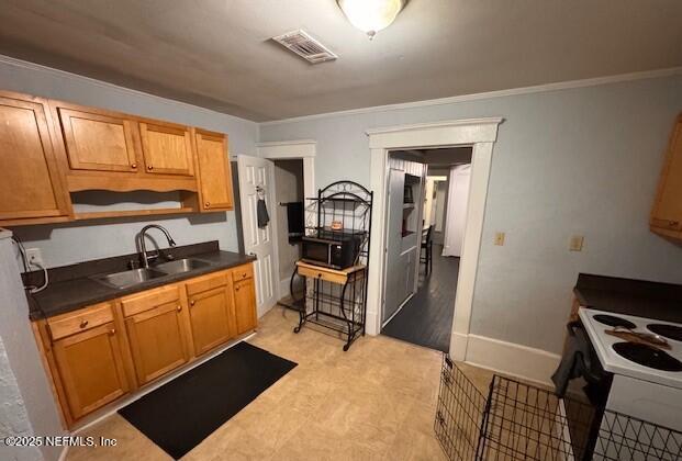 kitchen with electric range, a sink, visible vents, brown cabinets, and dark countertops