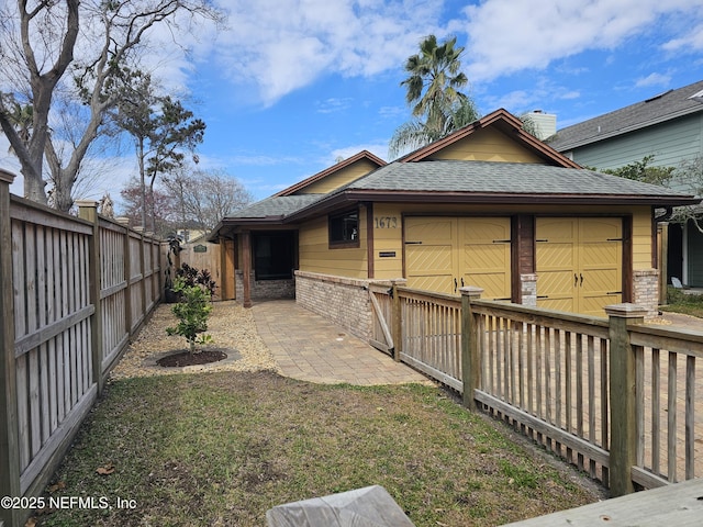 view of property exterior with a garage, a shingled roof, a fenced backyard, a patio area, and brick siding