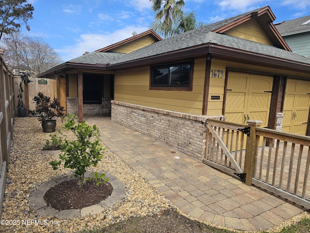 view of front of property featuring brick siding, a shingled roof, an attached garage, a patio area, and fence