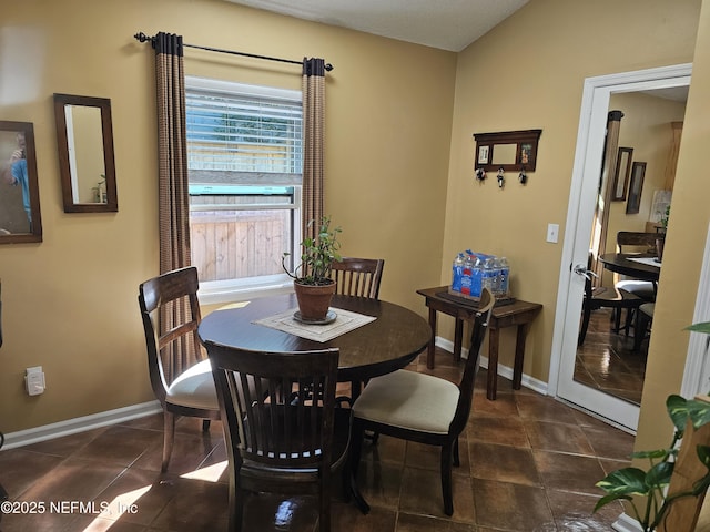 dining area featuring lofted ceiling, dark tile patterned floors, and baseboards