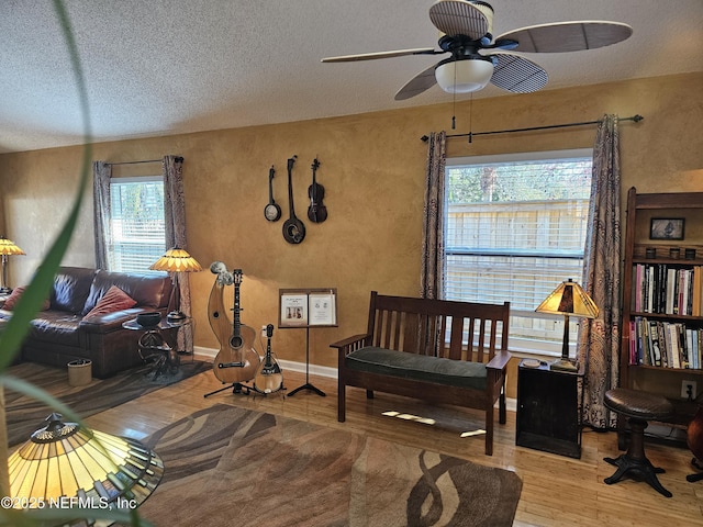 living area with a ceiling fan, a textured ceiling, baseboards, and wood finished floors