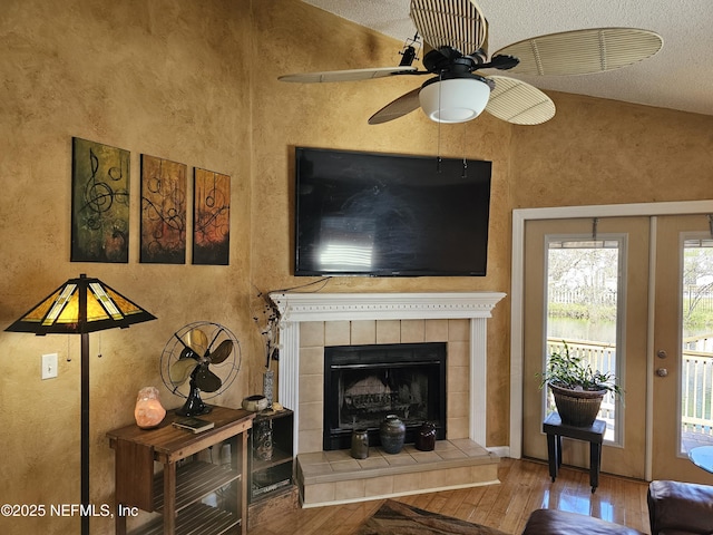 living area featuring lofted ceiling, a ceiling fan, hardwood / wood-style floors, and a tile fireplace