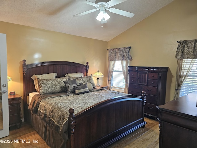 bedroom with vaulted ceiling, a textured ceiling, wood finished floors, and a ceiling fan