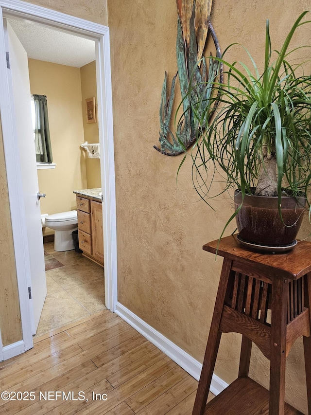 interior space featuring light wood-type flooring, a textured wall, and baseboards