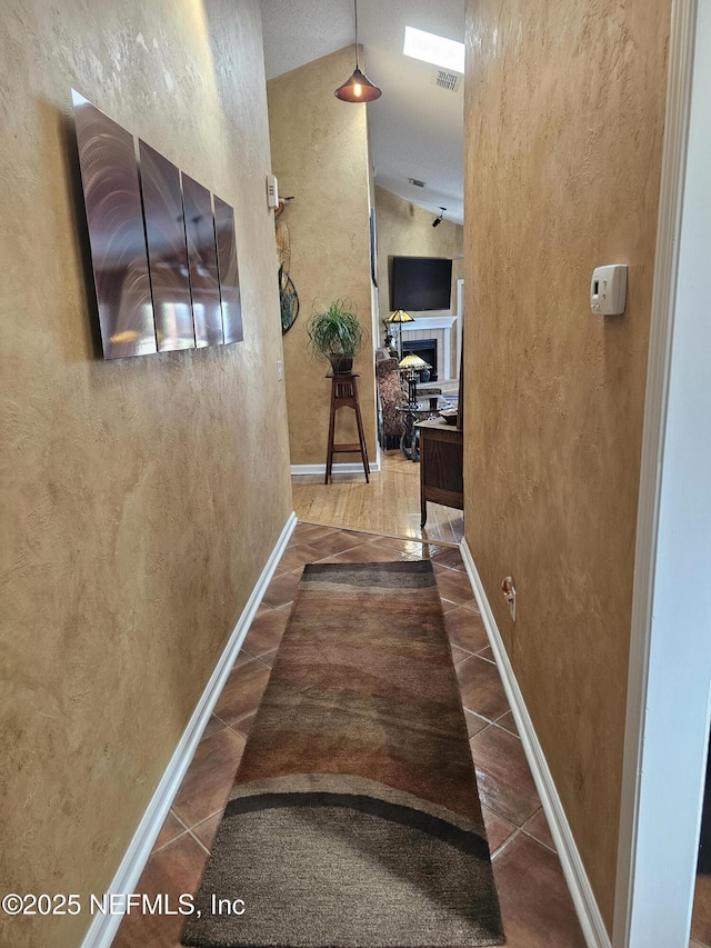 hall featuring a textured wall, high vaulted ceiling, visible vents, baseboards, and tile patterned floors