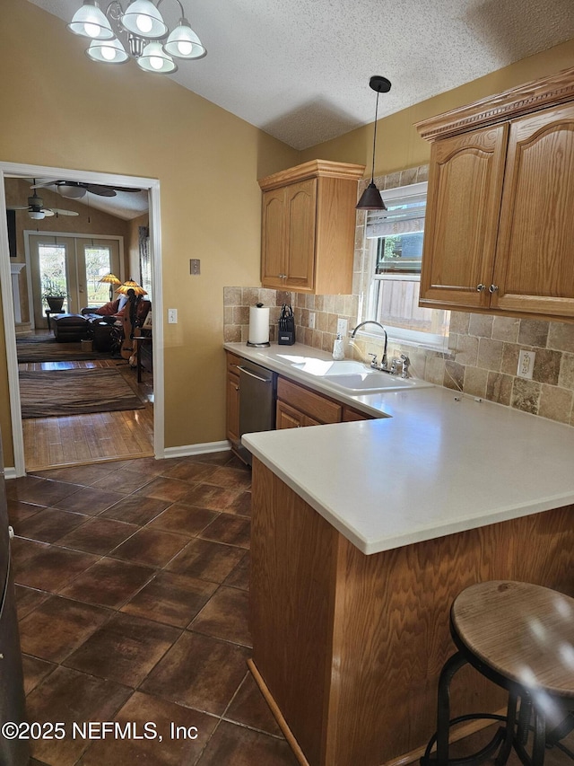 kitchen featuring a peninsula, a sink, vaulted ceiling, light countertops, and stainless steel dishwasher