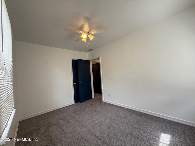 unfurnished room with dark colored carpet, a ceiling fan, visible vents, and baseboards