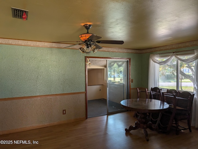 dining space with wallpapered walls, visible vents, wainscoting, a textured wall, and wood finished floors