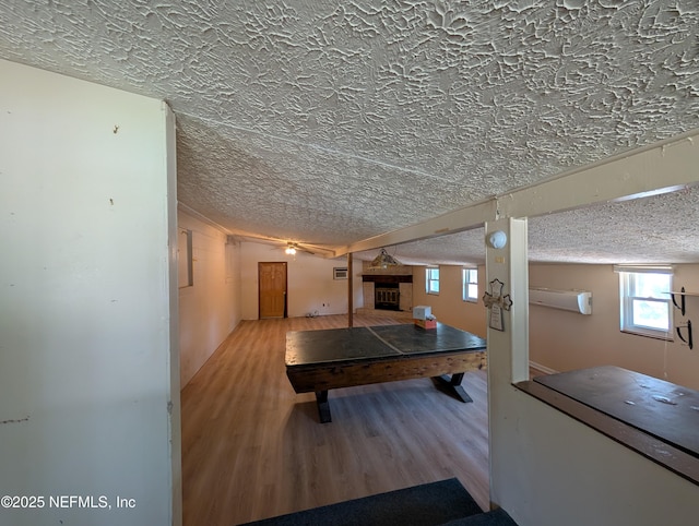 recreation room with a fireplace, a textured ceiling, and wood finished floors