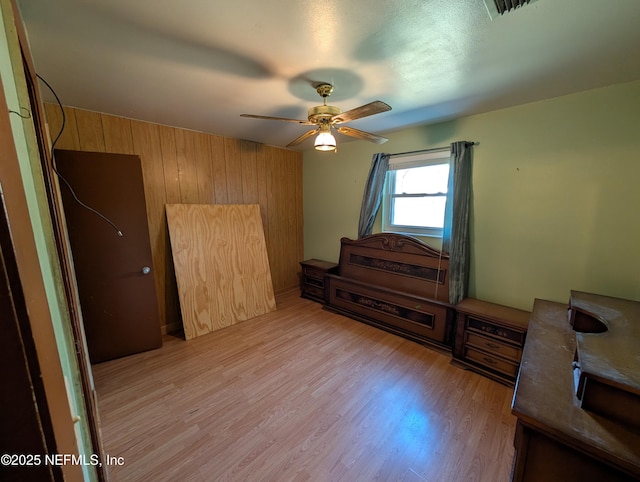 bedroom featuring wood walls, light wood-style flooring, visible vents, and a ceiling fan