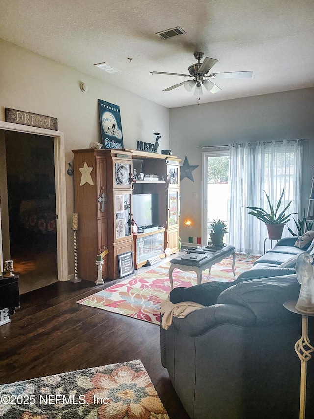 living room featuring dark wood-style floors, ceiling fan, a textured ceiling, and visible vents