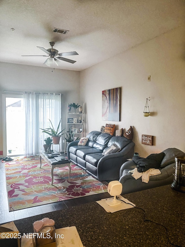 living area featuring ceiling fan, visible vents, and a textured ceiling