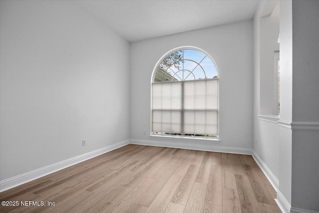 empty room with light wood-style flooring, baseboards, and a textured ceiling