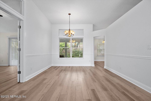 unfurnished dining area featuring light wood-type flooring, a notable chandelier, and baseboards