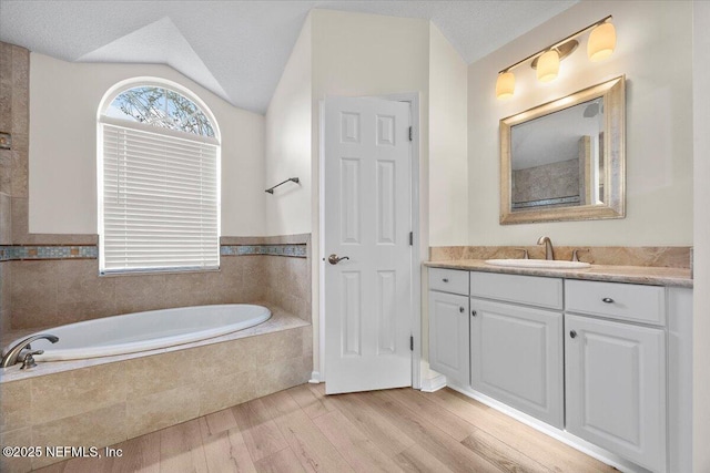 full bathroom featuring a garden tub, vaulted ceiling, vanity, a textured ceiling, and wood finished floors