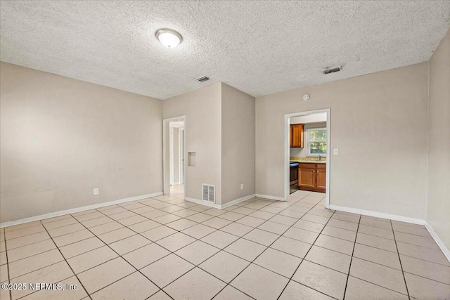 spare room featuring light tile patterned floors, a textured ceiling, visible vents, and baseboards