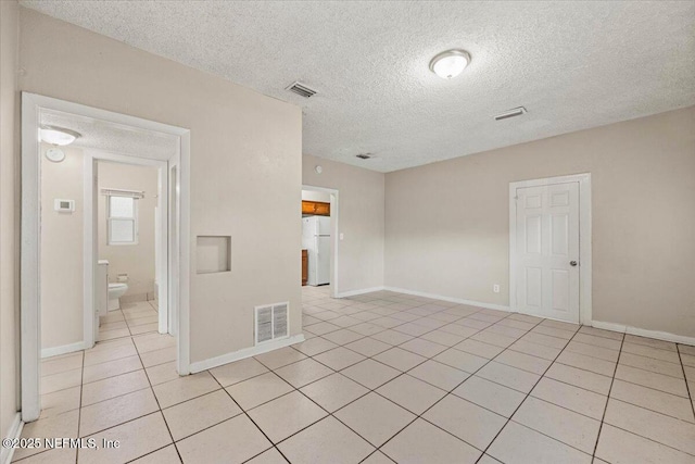 spare room featuring visible vents, a textured ceiling, baseboards, and light tile patterned floors