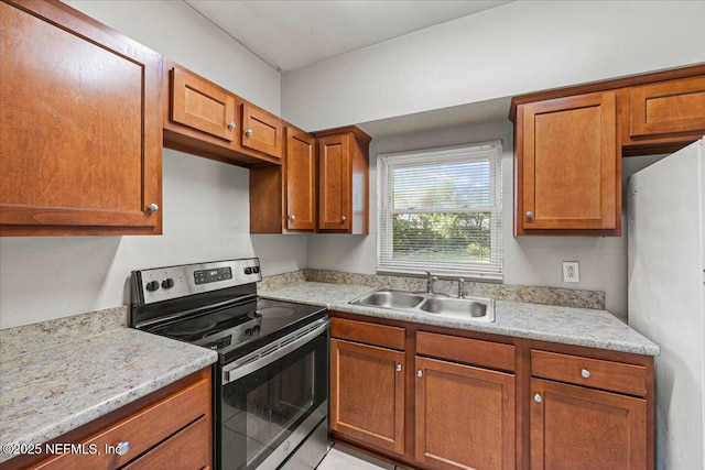 kitchen with stainless steel electric range, brown cabinets, a sink, and freestanding refrigerator