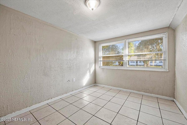 spare room featuring light tile patterned floors, baseboards, a textured ceiling, and a textured wall