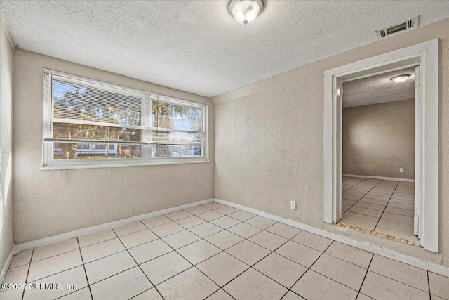 empty room featuring tile patterned flooring, visible vents, a wealth of natural light, and a textured wall