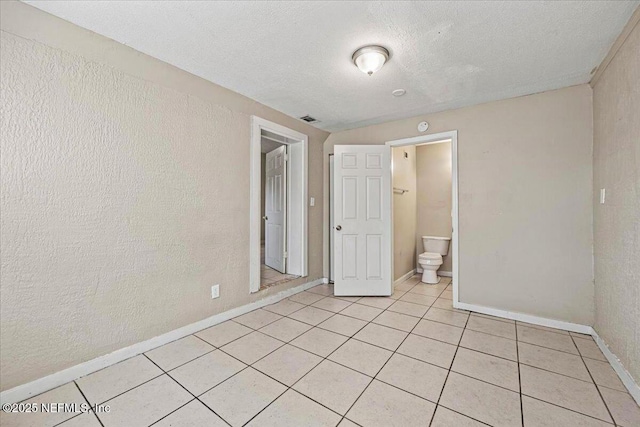 unfurnished bedroom featuring light tile patterned floors, visible vents, a textured wall, a textured ceiling, and baseboards