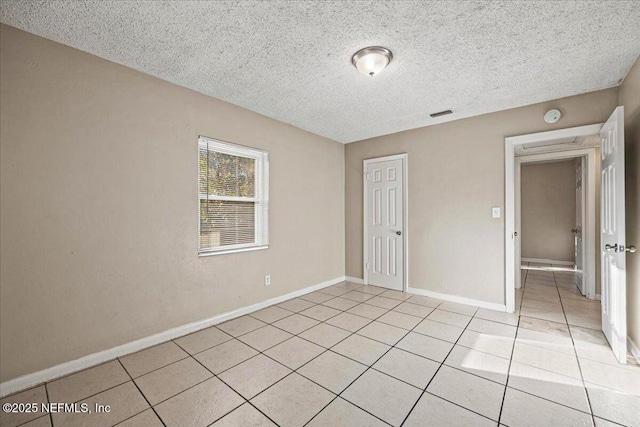 spare room featuring visible vents, a textured ceiling, baseboards, and light tile patterned floors