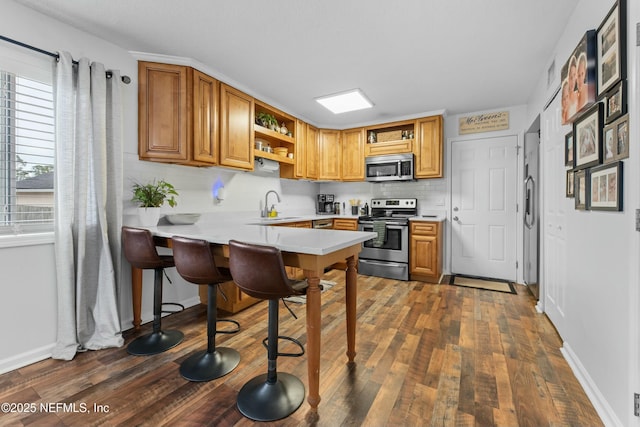 kitchen featuring open shelves, stainless steel appliances, light countertops, a sink, and a peninsula