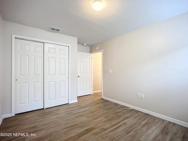 unfurnished bedroom with a textured ceiling, a closet, wood finished floors, and visible vents