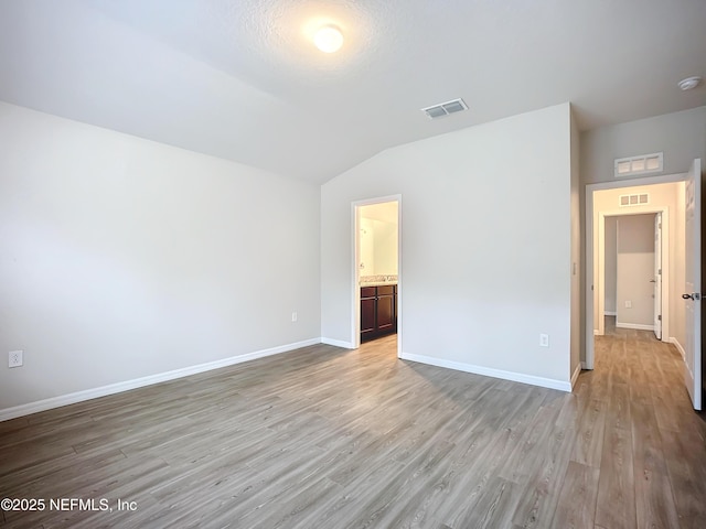 interior space with light wood-style flooring, visible vents, vaulted ceiling, and baseboards